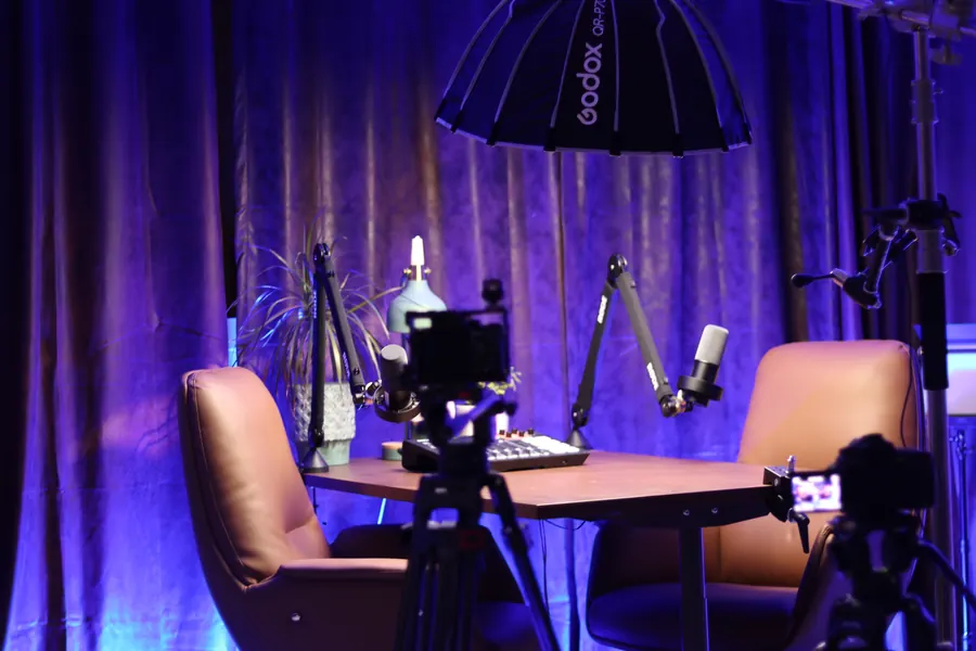 Our studio set for a two-person interview: two chairs at a table with microphones, two cameras on tripods and a softbox overhead