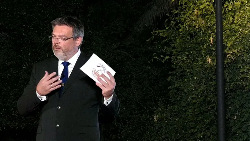 Camera two: a close shot of the same speaker holding an envelope, recorded at the same moment